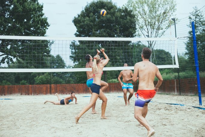Spielbetrieb Ein Beachvolleyballspiel mit mehreren Männern im Sand. Bäume im Hintergrund.